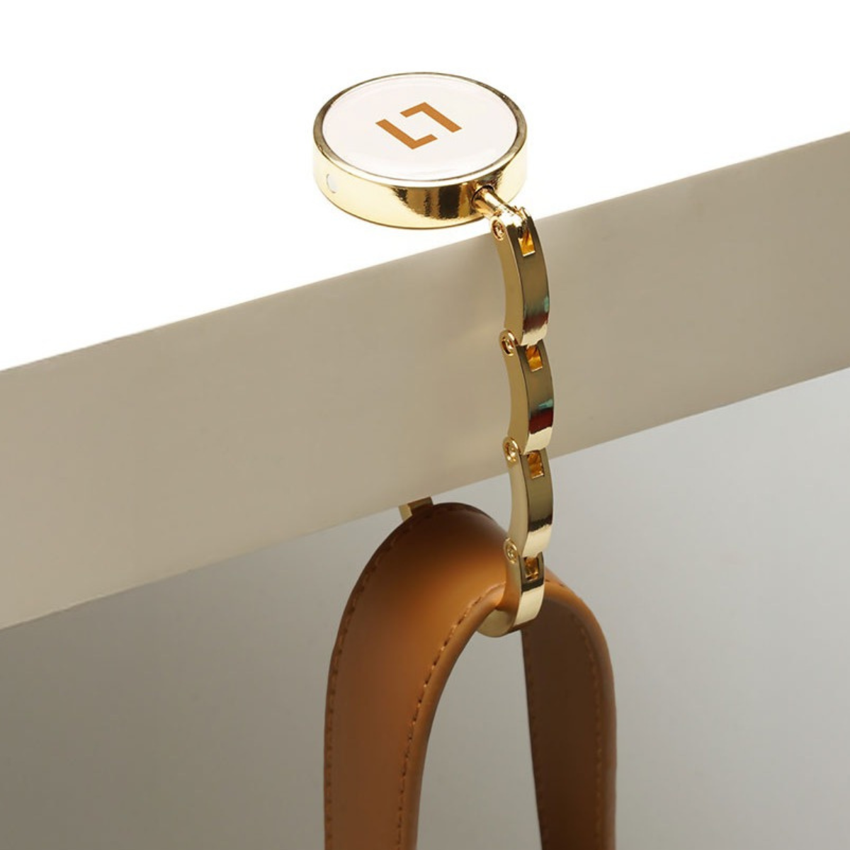 Gold handbag handle with a logo on a neutral background