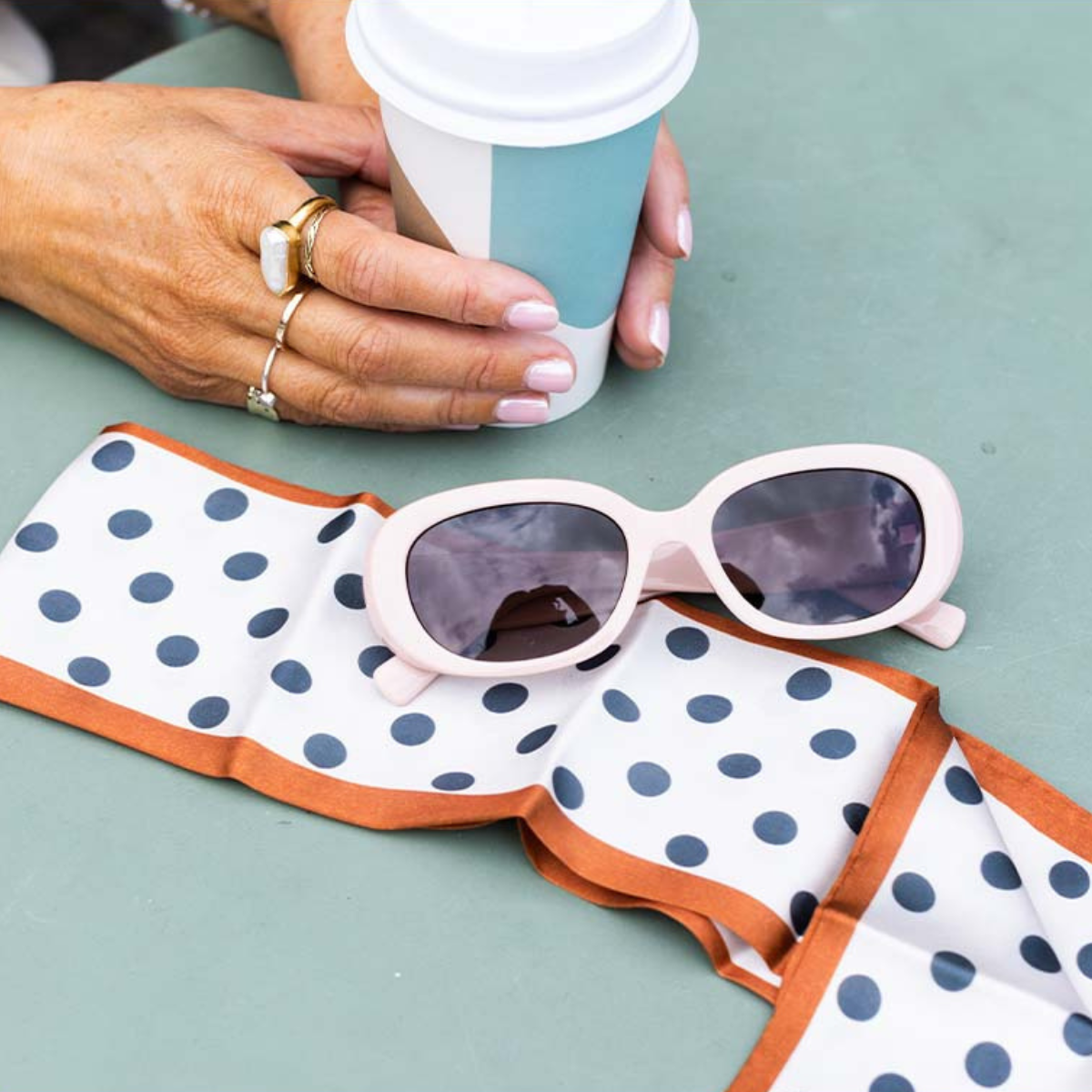 Sunglasses on a polka dot napkin with a hand holding a coffee cup in the background