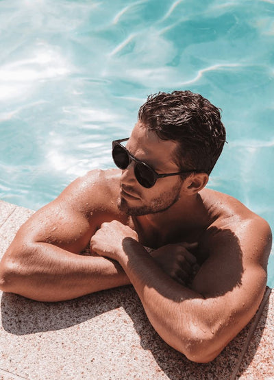Man relaxing by a pool wearing Bask sunglasses